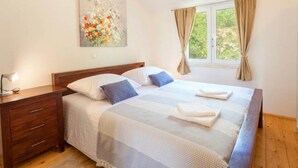 Une chambre à coucher comprenant un lit, une table de chevet, une commode, une fenêtre avec des rideaux et un tableau accroché au mur.