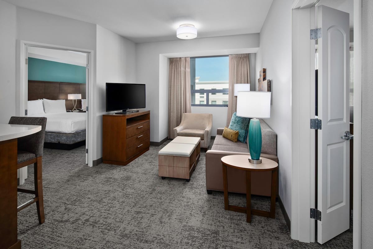 A hotel room with a bed, a TV, a sofa, a small table, and a window with curtains.