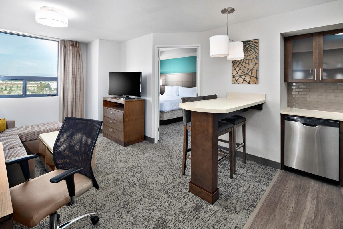 Habitación de hotel con cama, televisión, escritorio con silla, zona de comedor y cocina.