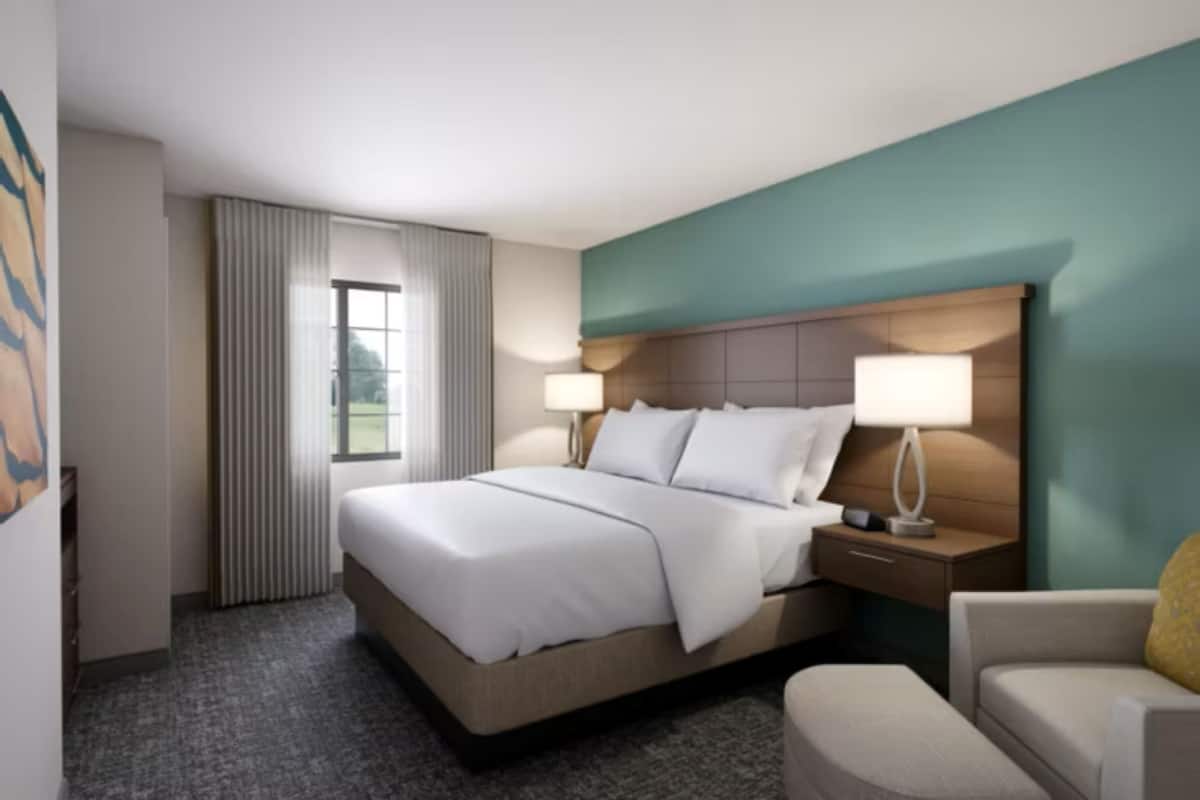 A hotel room with a large bed, two bedside tables with lamps, a chair, and a window with curtains.