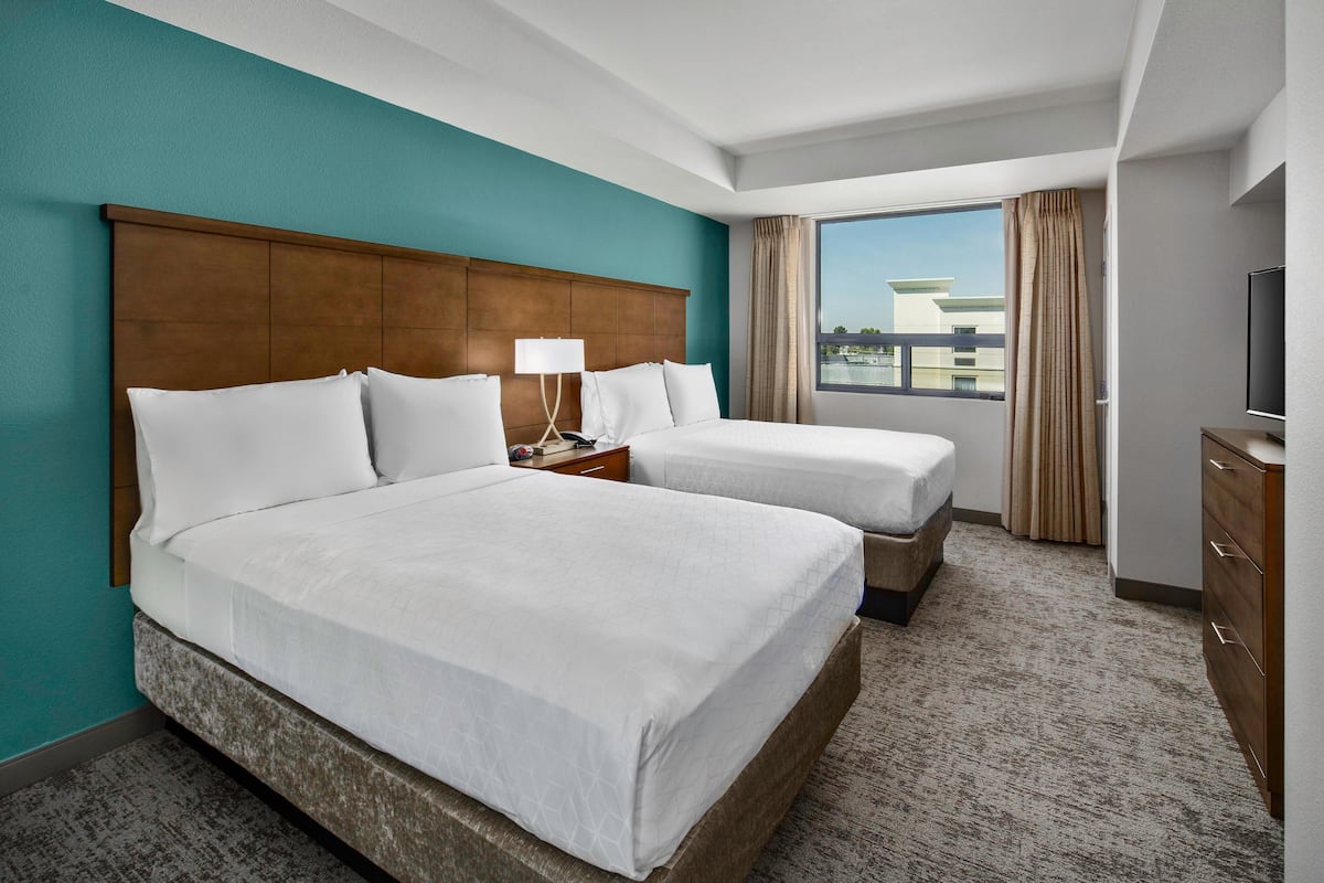 A hotel room with two beds, a large window, a television, and a wooden headboard.
