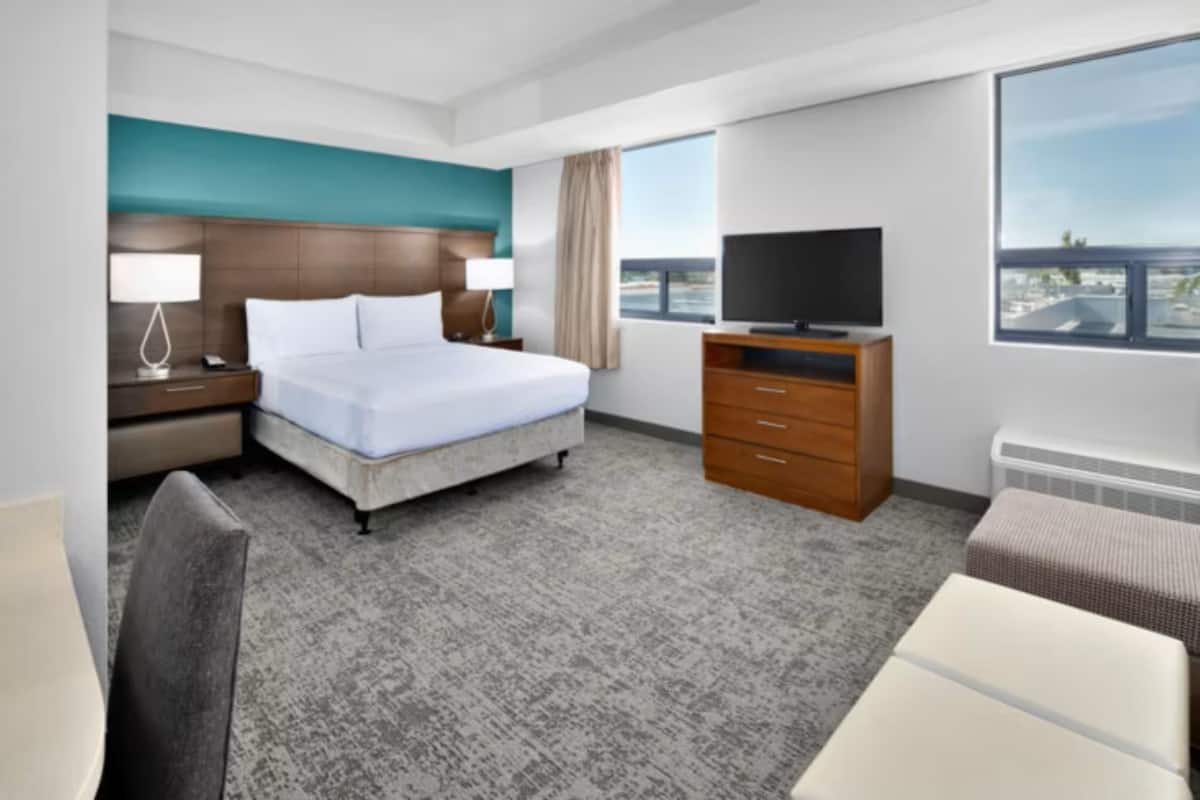 A hotel room with a bed, a TV, a dresser, a chair, and a window with a view.