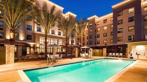 A hotel pool area with a clear pool, palm trees, and a well-lit building facade. - Staybridge Suites Irvine - John Wayne Airport IHG (Costa Mesa)