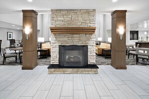 Un vestíbulo moderno con chimenea de piedra, columnas de madera y una zona de estar con sofás y mesas.