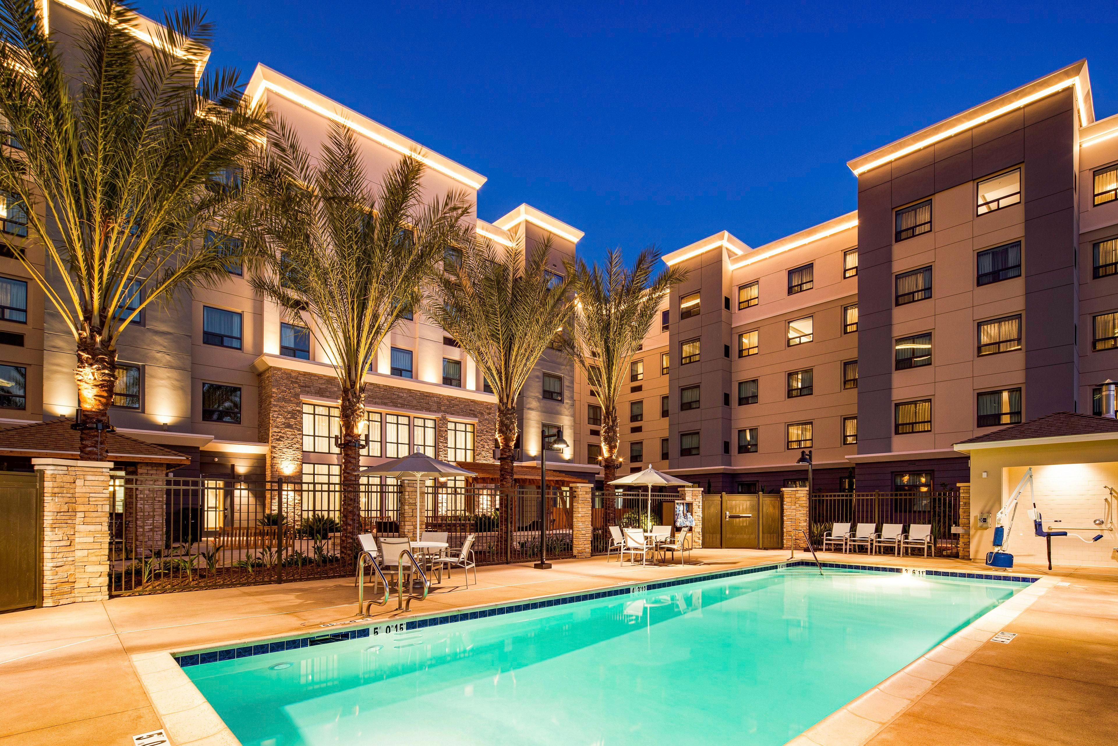 A hotel pool area with a clear pool, palm trees, and a well-lit building facade.