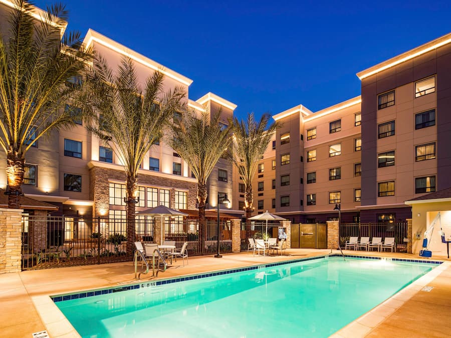 A hotel pool area with a clear pool, palm trees, and a well-lit building facade.