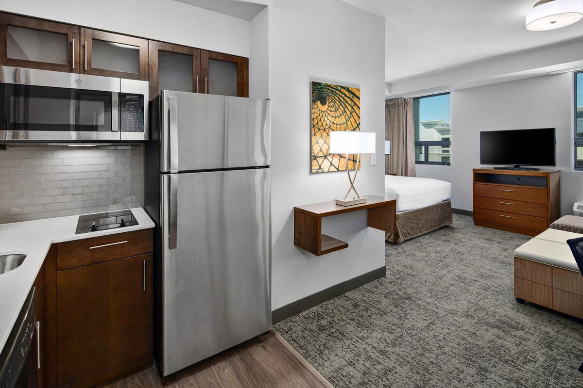 Una habitación de hotel moderna con kitchenette, una cama, un televisor y una ventana con vistas.