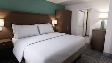 Una habitación de hotel con una cama grande, cabecera de madera, dos lámparas de noche, una mesita de noche, un armario y una puerta que da a un baño.