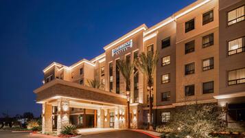 Een Staybridge Suites hotel met een moderne gevel, een overdekte ingang en palmbomen.