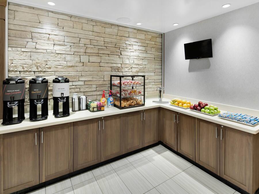 Una cocina moderna con protector de piedra, cafeteras, una exposición de frutas y un televisor de pantalla plana.