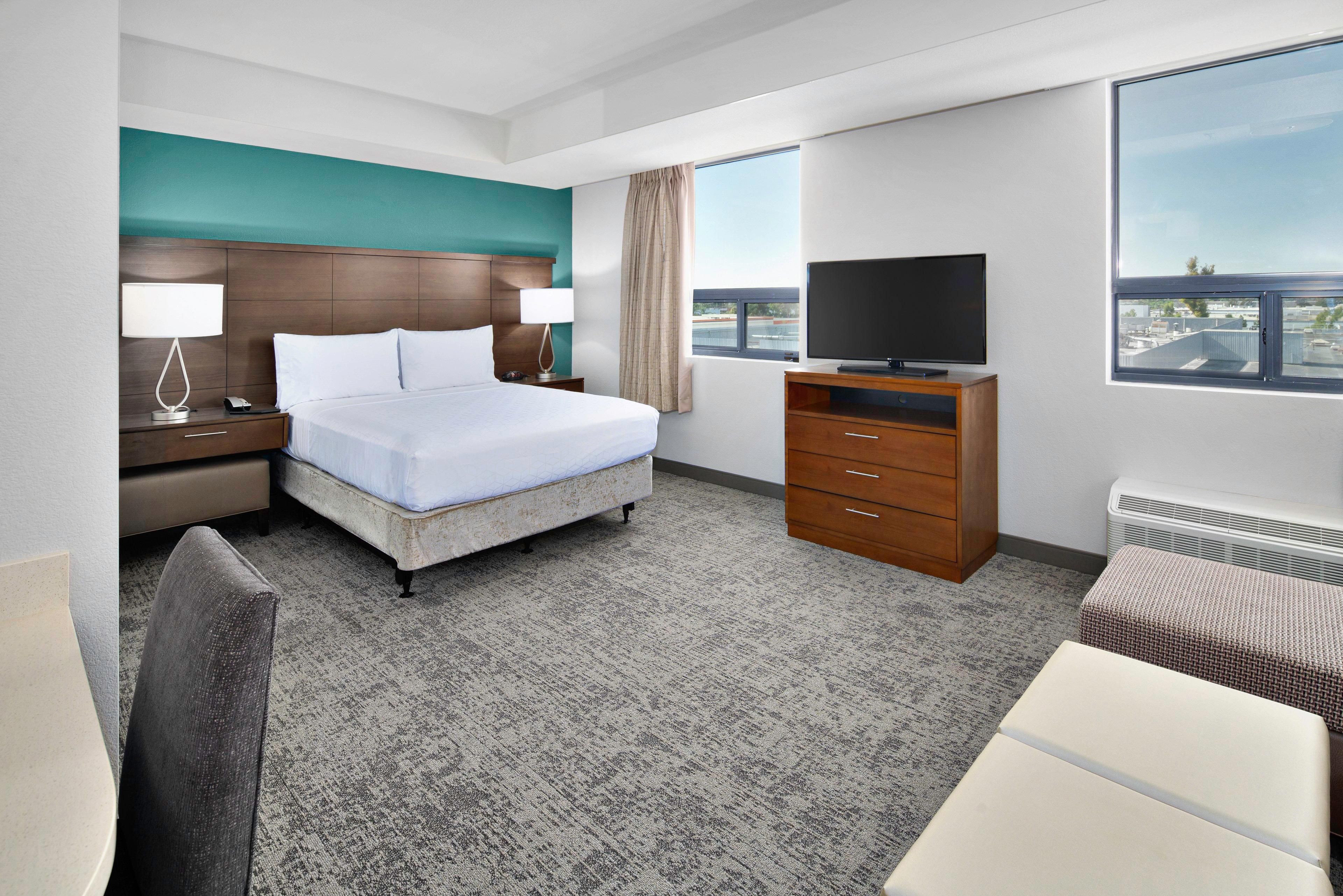 A hotel room with a bed, a TV, a desk, and a view of the city.