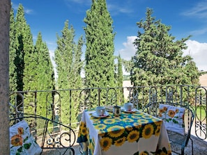 A table set outdoors with a sunflower tablecloth, surrounded by metal chairs with floral cushions, overlooking a forested area. - A Spacious Retreat for Ten (Sarteano)
