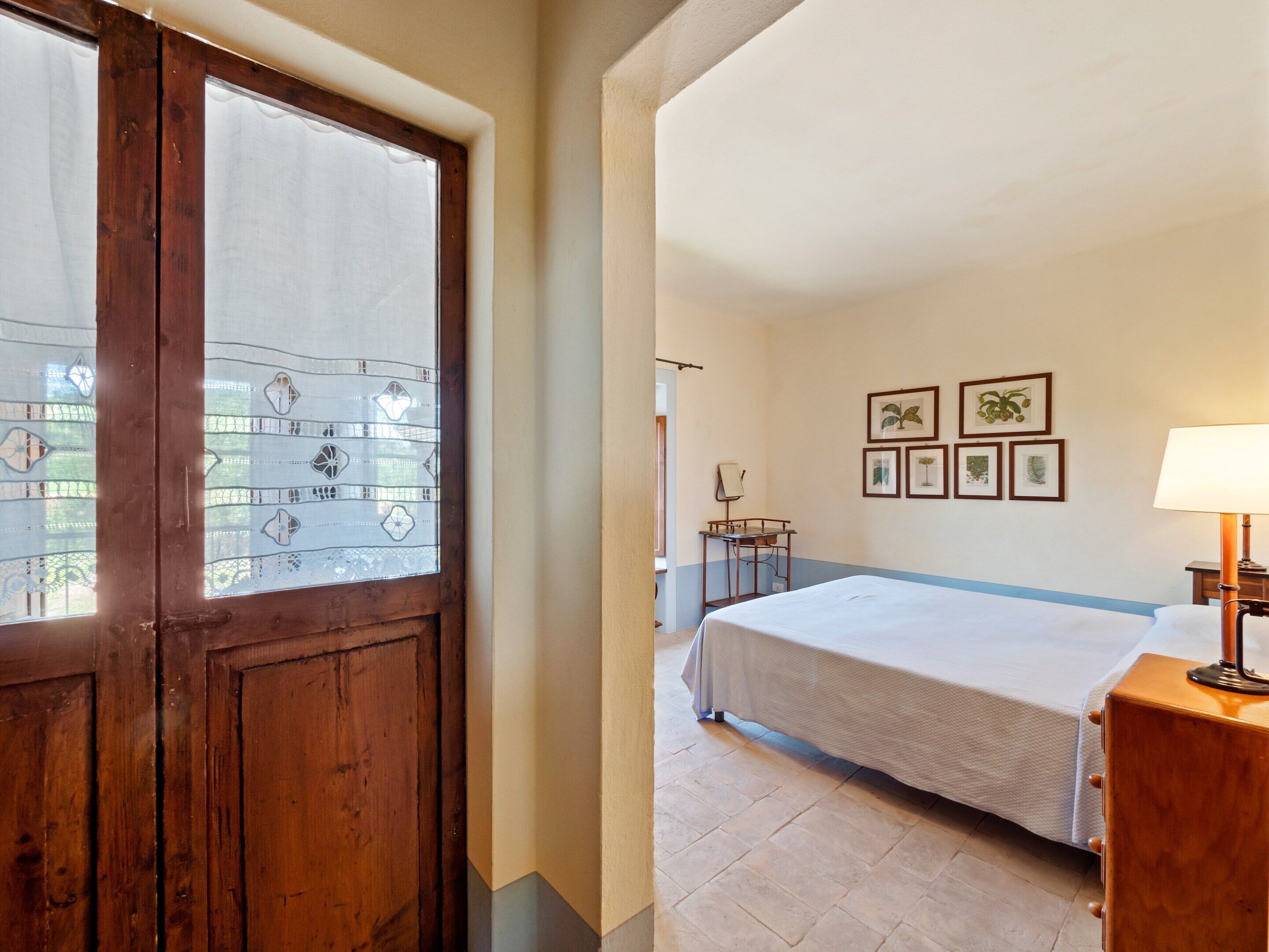 A hotel room with a bed, a desk, and a chair. There are framed pictures on the wall.