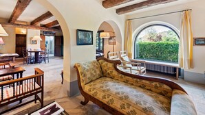Una habitación acogedora con vigas de madera a la vista, un amplio ventanal con vistas a la vegetación, un sofá floral y un comedor con mobiliario de madera.