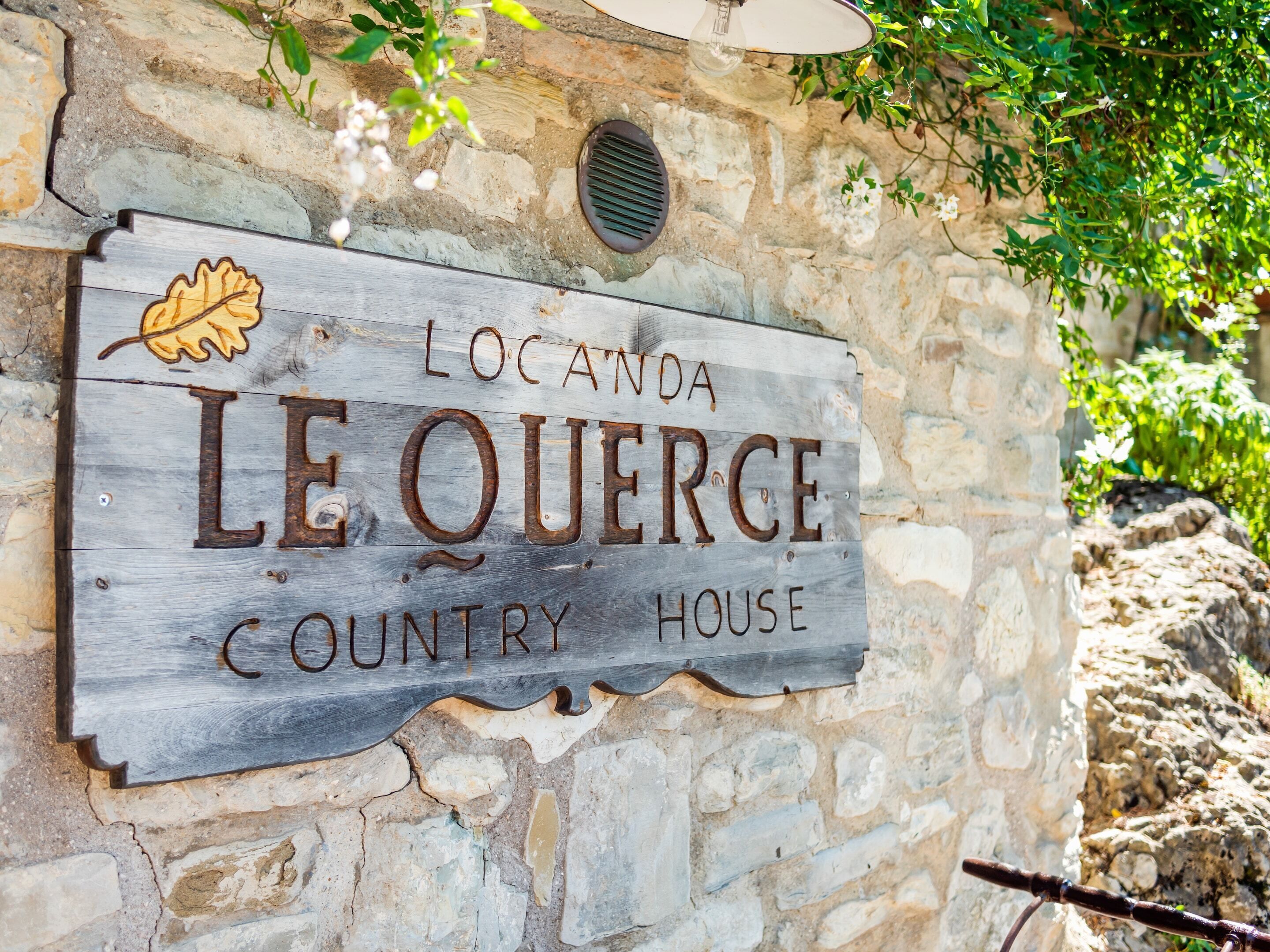 A rustic wooden sign with the text "Locanda Le Querce Country House" mounted on a stone wall.