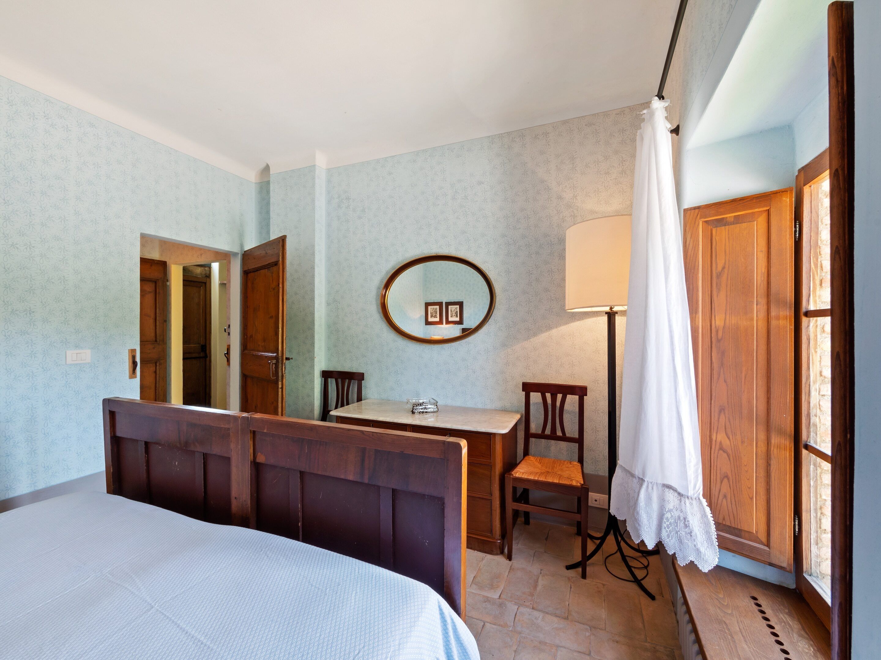 A bedroom with a bed, a desk, a chair, a lamp, and a window with curtains.