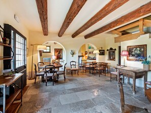Un vaste espace dédié à la salle à manger, avec des tables et des chaises en bois, un sol en pierre et des poutres apparentes en bois au plafond.