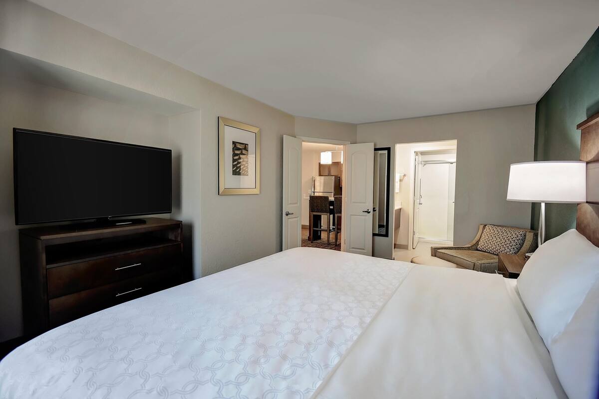 A hotel room with a large bed, a TV on a wooden dresser, a chair, and a lamp.