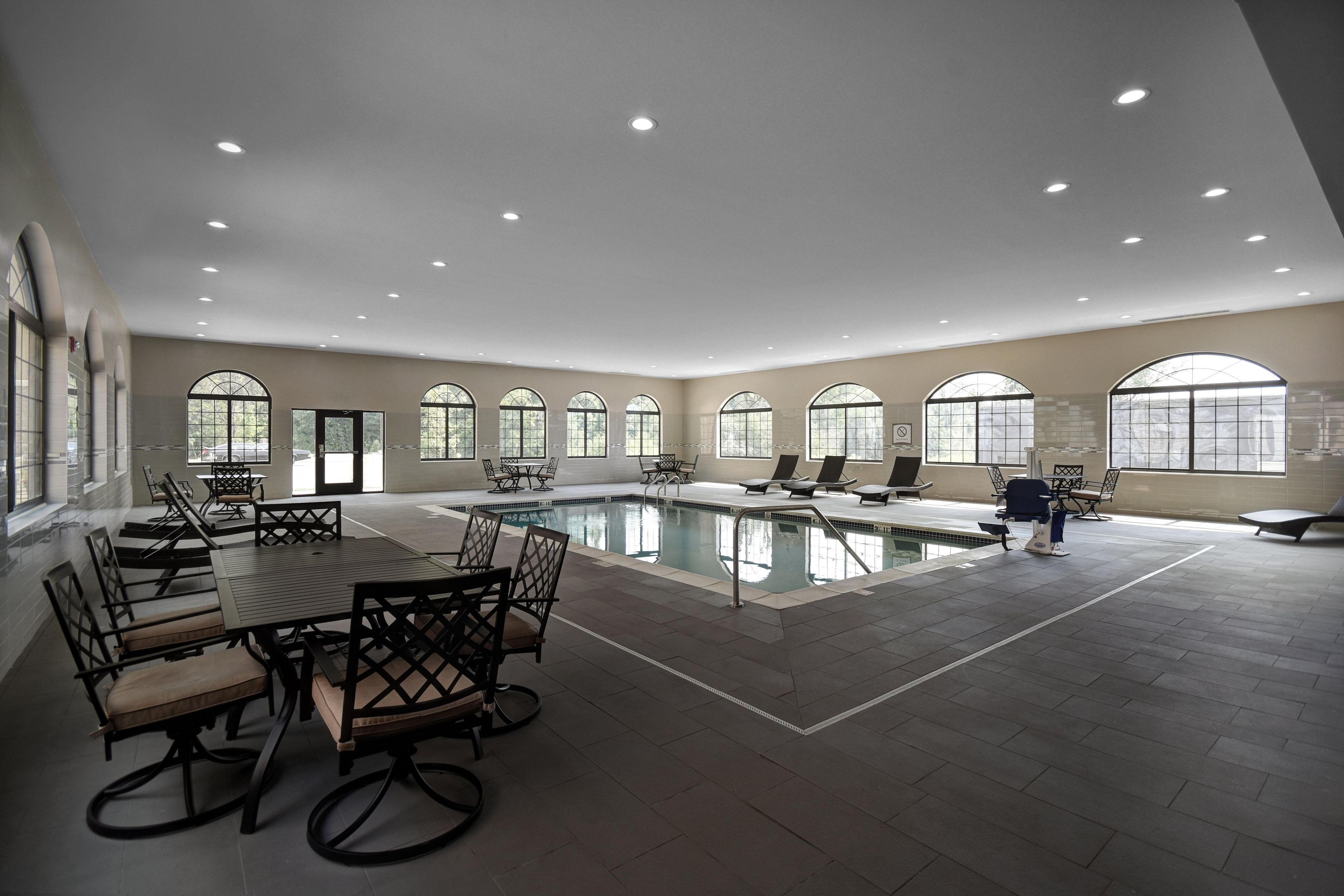 A spacious indoor swimming pool area with multiple seating arrangements and large windows.