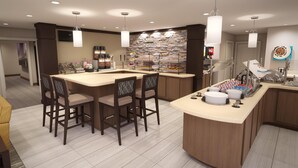 A modern kitchen with a central island, bar stools, and a variety of food items displayed on shelves. - Staybridge Suites Holland (Holland)