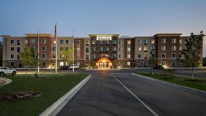 A Staybridge Suites hotel with a central entrance, multiple floors, and a well-maintained lawn. - Staybridge Suites Holland (Holland)