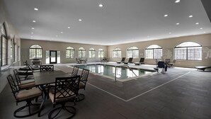 Amplia zona de piscina interior con diversas opciones de asientos y grandes ventanales.