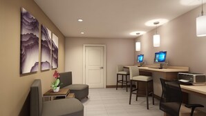 A modern hotel room with a reception desk, two computer monitors, a printer, and a seating area with chairs and a small table. - Staybridge Suites Holland (Holland)