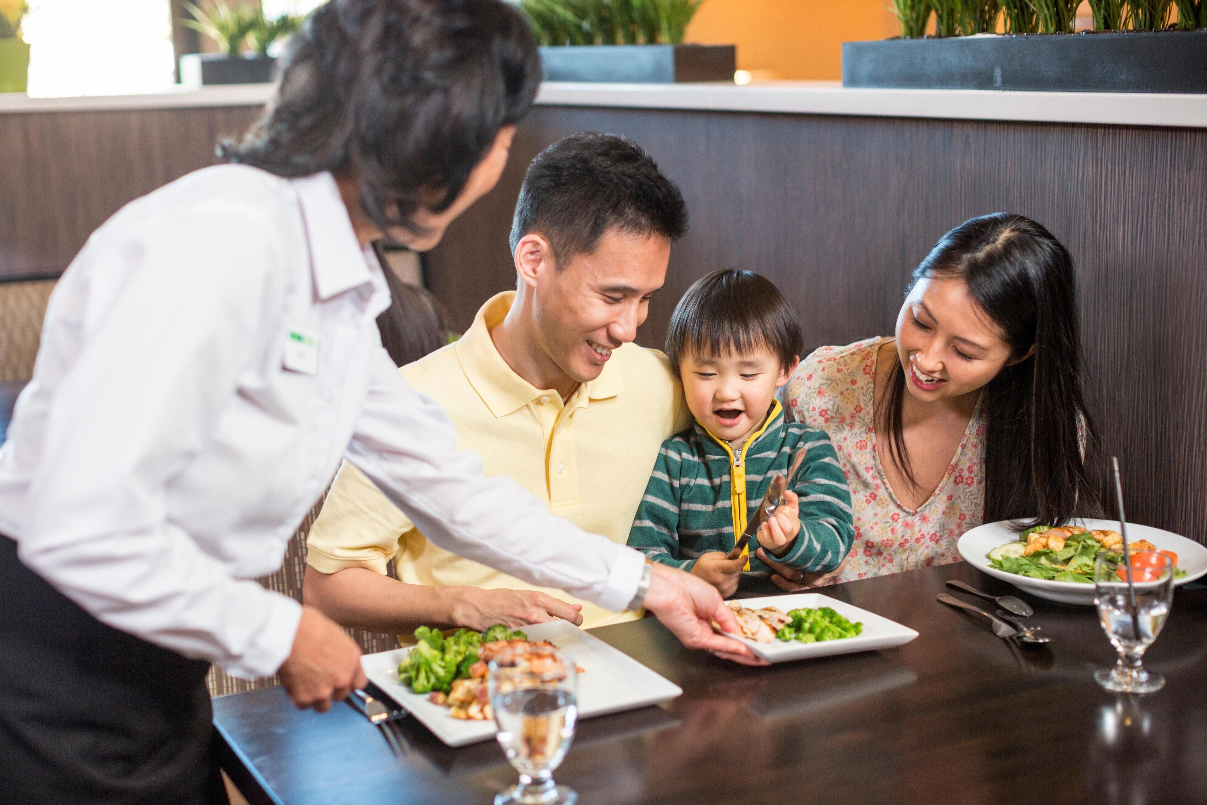 A family dining at a restaurant with a waiter serving food.