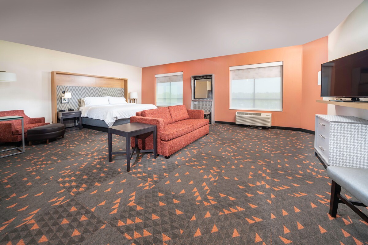 A hotel room with a bed, a sofa, a desk, a television, and a large window.