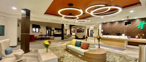 A hotel lobby with a reception desk, seating area, and a modern ceiling design.