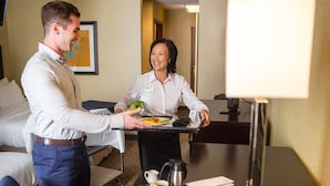 A hotel room with a bed, a desk, a laptop, a coffee maker, and a tray with food and a plant. - Holiday Inn St. Louis - Creve Coeur (St. Louis)
