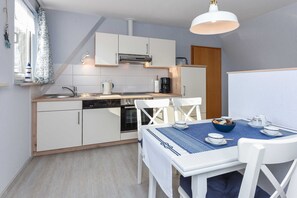 A compact kitchen with white cabinetry, a built-in oven, and a dining area with a table set for two.