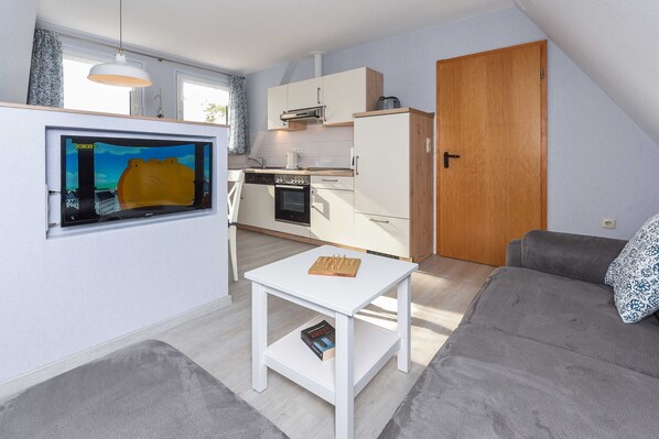 A compact living space with a kitchenette, a dining table, a sofa, and a television mounted on the wall.