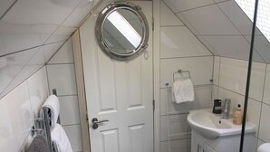 Een kleine, moderne badkamer met een witte deur, een ronde spiegel, een wastafel met toiletartikelen en een handdoekrek.