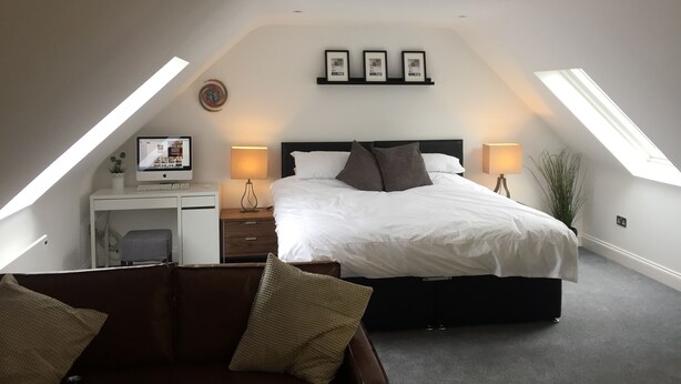 Een slaapkamer met een bed, een bureau met een computer en twee lampen. Er zijn dakramen in het plafond.