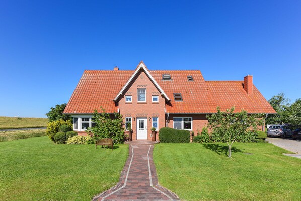 A two-story brick house with a red-tiled roof, a central entrance, and a paved pathway leading to the door.