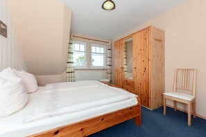 Une chambre à coucher avec un lit en bois, une armoire en bois, une chaise et une fenêtre avec des rideaux.