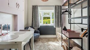 Une pièce moderne avec une table blanche, un canapé bleu, un radiateur, une fenêtre avec des rideaux et un étagère suspendue avec des boîtes de rangement.