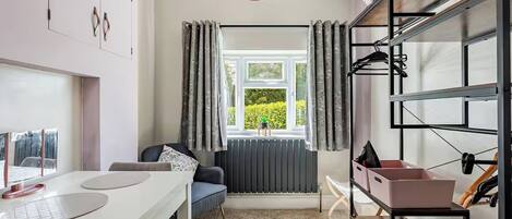 A modern room with a white table, a blue sofa, a radiator, a window with curtains, and a hanging rack with storage boxes.