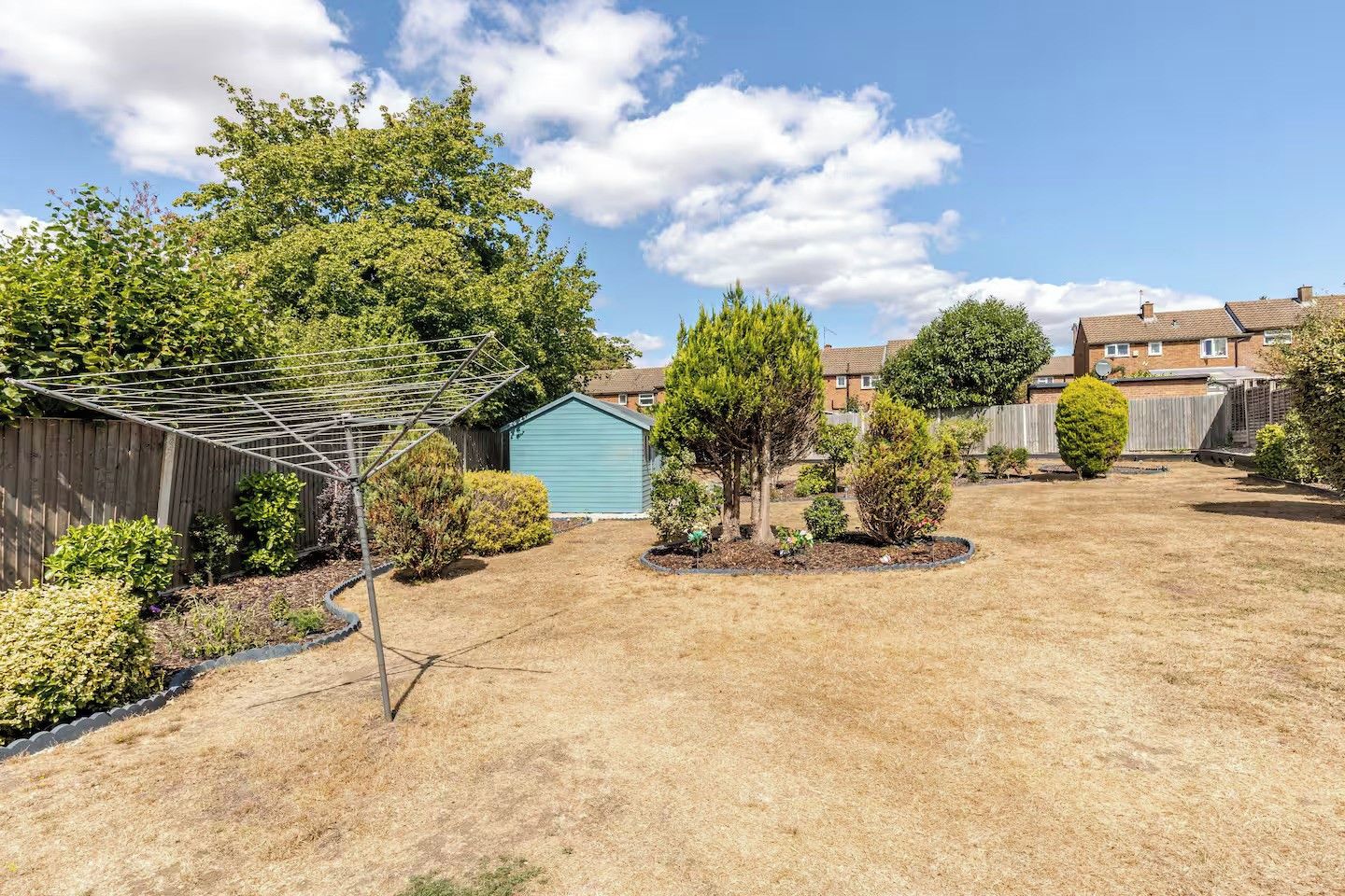 Ein Garten mit Blumenbeet, Gartenhaus und Rasenfläche.