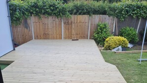 Una terraza de madera con un cerco de madera y follaje al fondo.