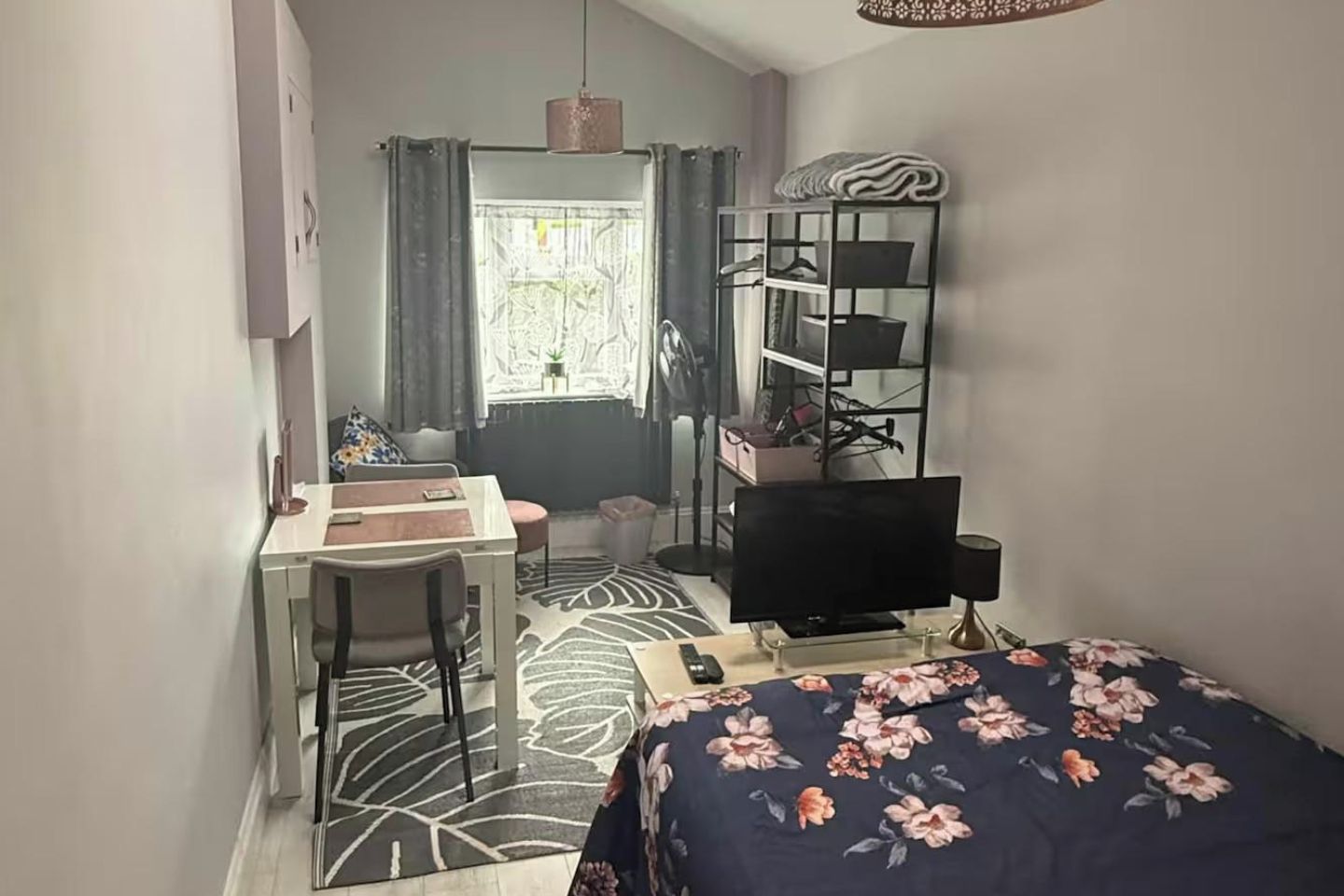 Una habitación compacta con cama, escritorio, silla, televisor y ventana con cortinas.