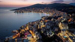 An aerial view of a coastal city at dusk with a well-lit waterfront and dense urban development. - Art Hotel (Sarandë)