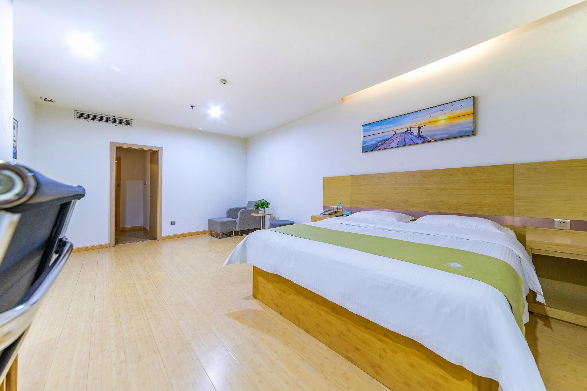 Habitación de hotel con cama, escritorio, silla, pequeña mesa con una planta y un cuadro en la pared.