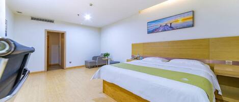 Habitación de hotel con cama, escritorio, silla, pequeña mesa con una planta y un cuadro en la pared.