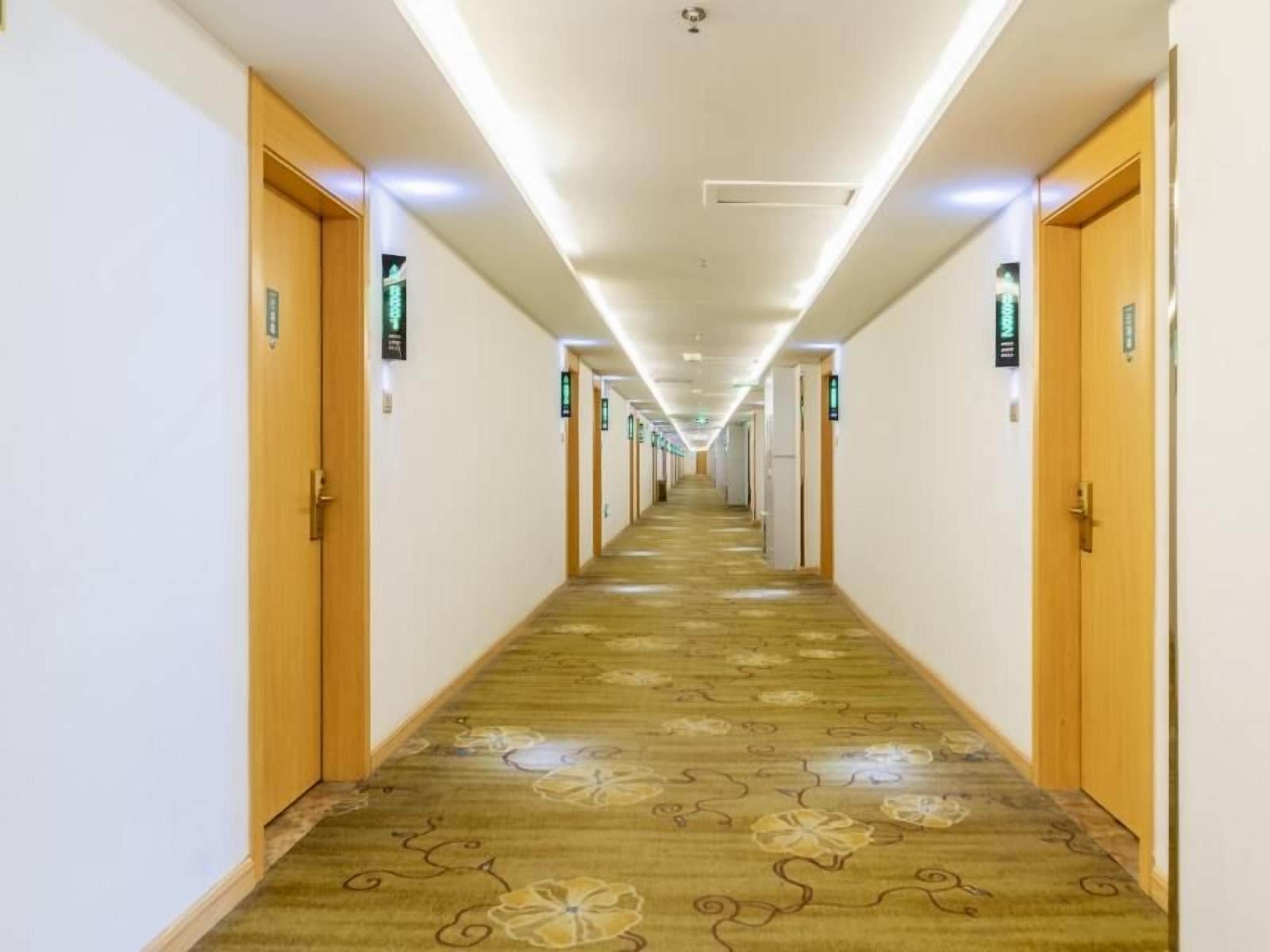 Un pasillo de hotel con puertas de madera, suelo alfombrado e iluminación en el techo.