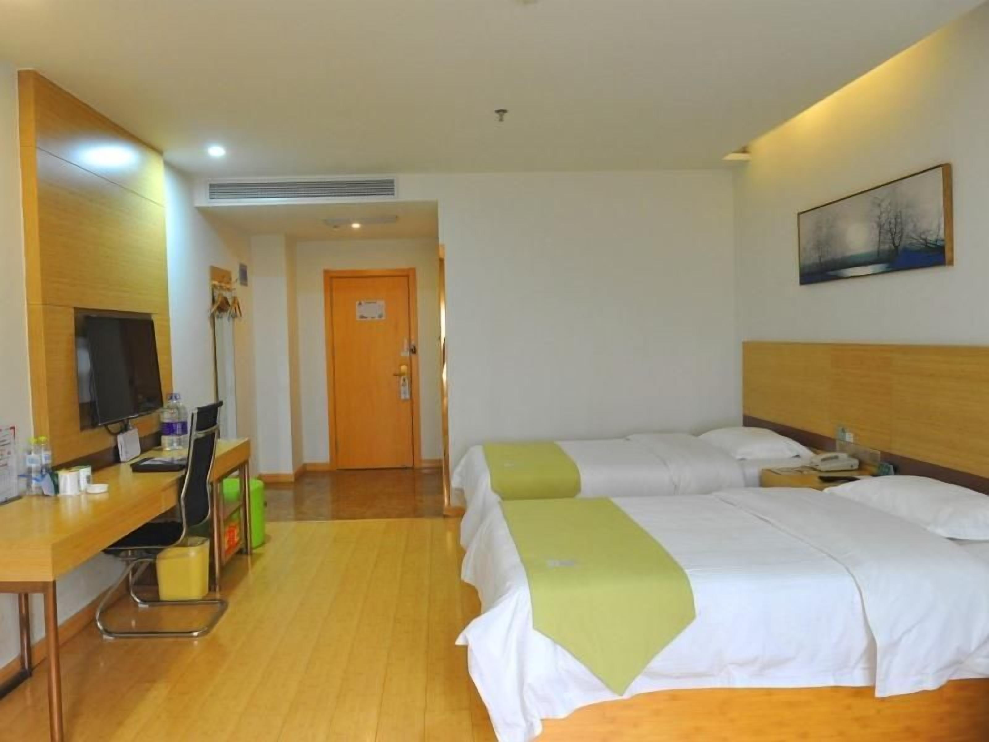 A hotel room with two beds, a desk with a computer, a television, and a door leading to another room.