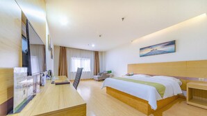 A hotel room with a wooden desk, a bed with a green and white bedspread, a nightstand, a chair, and a painting on the wall. - Greentree Alliance Liaocheng Dongchangfu District Chenkou Road Liaocheng University Hotel (Liaocheng)