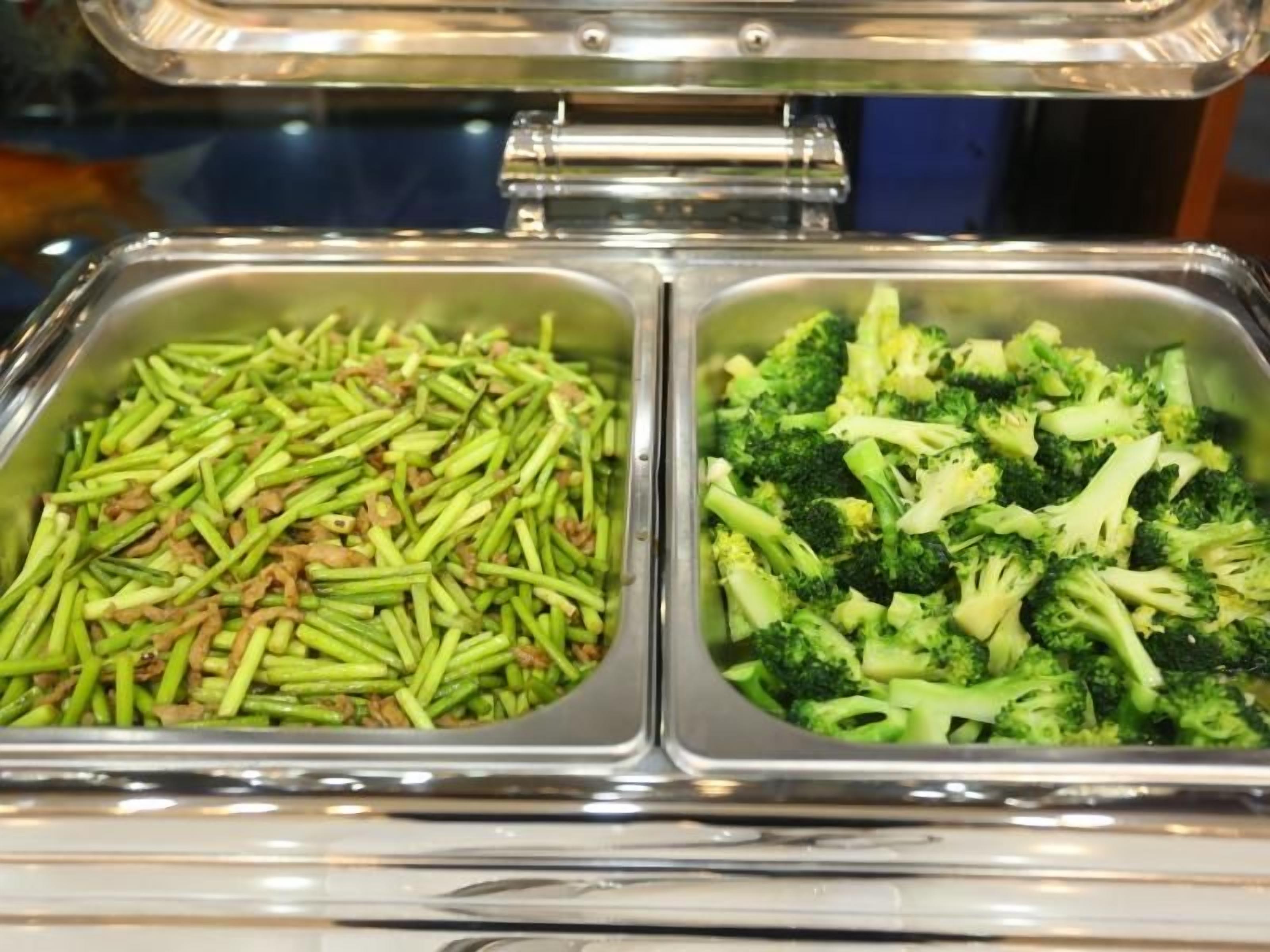 Dos dispensadores de acero inoxidable con verduras verdes, uno con ejotes y otro con brócoli.