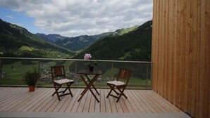 A wooden deck with two chairs and a table, overlooking a mountainous landscape.